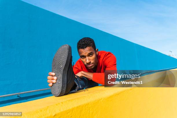 young dancer stretching on yellow wall - black men feet stock-fotos und bilder