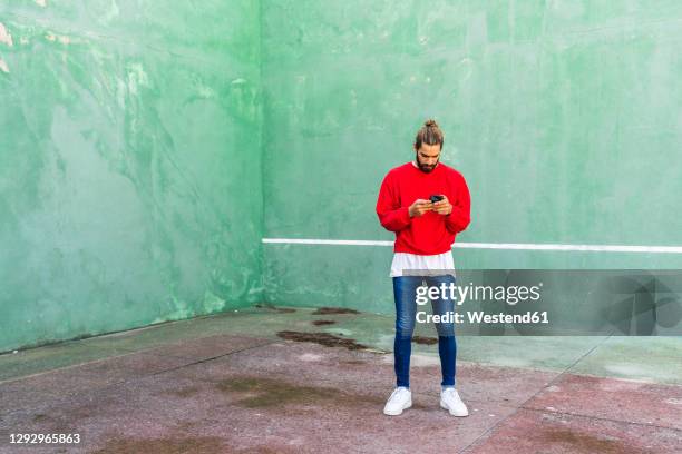 young man wearing red sweatshirt raising hands in front of green wall - sweatshirt fotografías e imágenes de stock