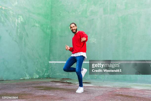 portrait of bearded young man dancing in front of green wall - dancer foto e immagini stock