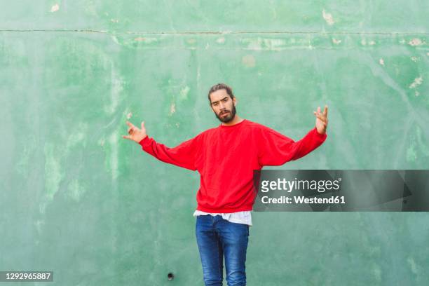 portrait of angry young man wearing red sweatshirt in front of green wall - sweatshirt stock-fotos und bilder
