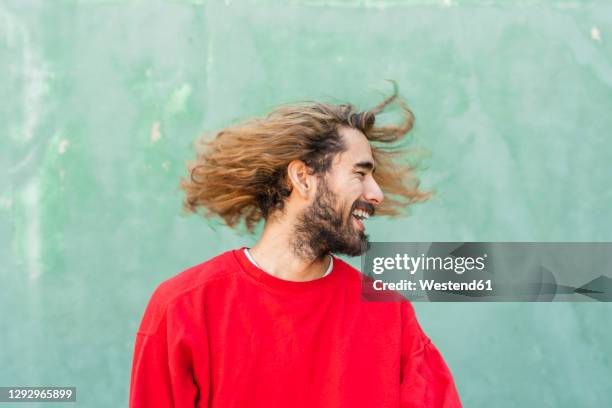 bearded young man with tossing his hair in front of green wall - men hair stock pictures, royalty-free photos & images