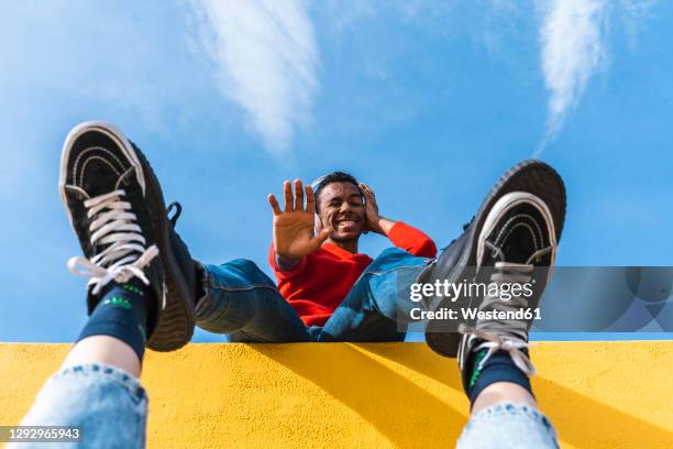 young man with headphones, dancing for person, leaning on yellow wall - ballerina feet stockfoto's en -beelden