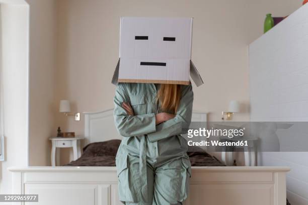 woman wearing a cardbox on head with bored smiley leaning on bed at home - schizophrenia stock pictures, royalty-free photos & images