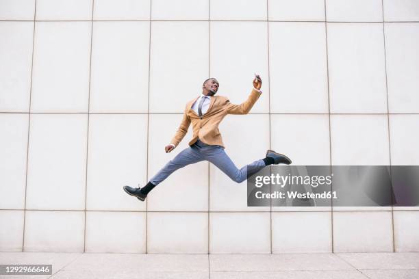 young businessman jumping and taking a selfie in front of a wall - business freedom stock pictures, royalty-free photos & images