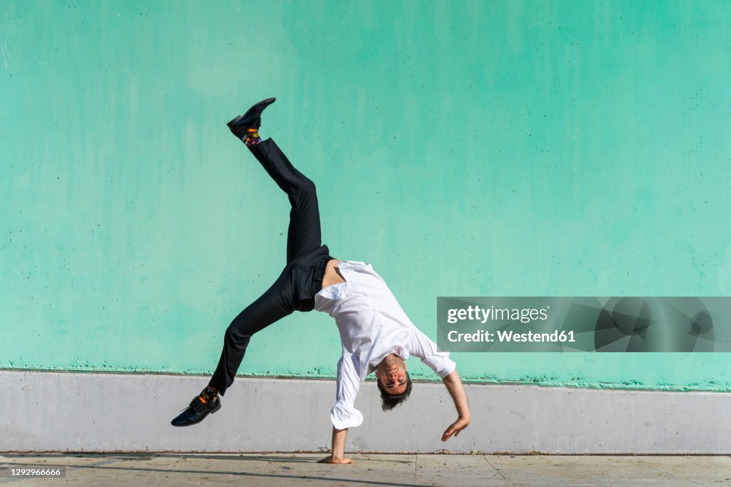 Businessman doing handspring in front of green wall