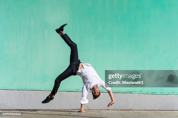 businessman doing handspring in front of green wall - cartwheel stock pictures, royalty-free photos & images