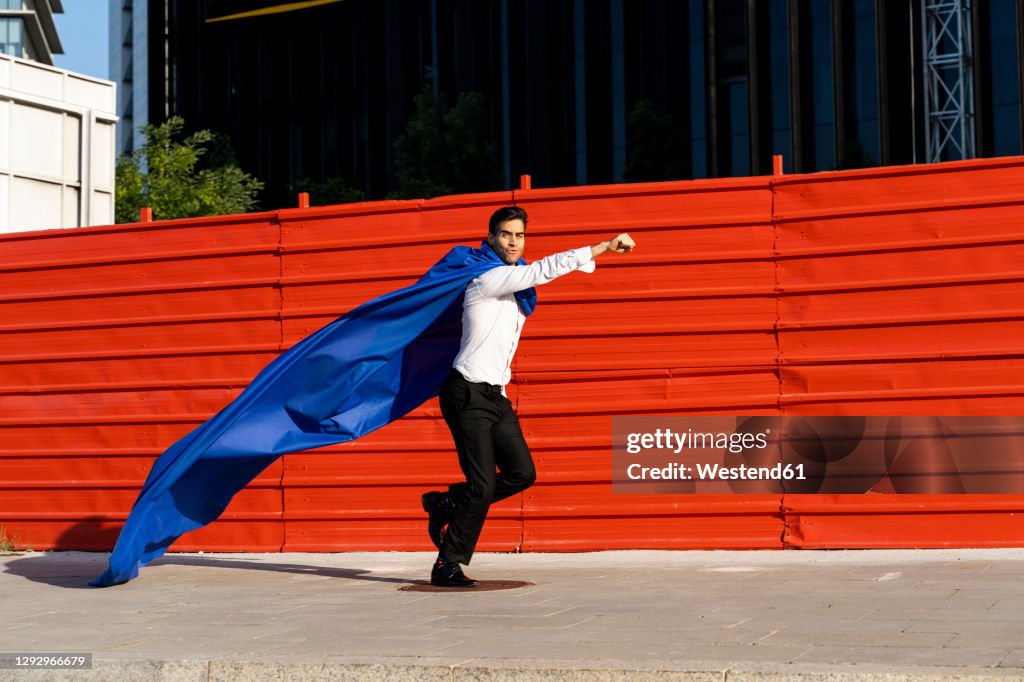 Businessman wearing superhero cape running on pavement