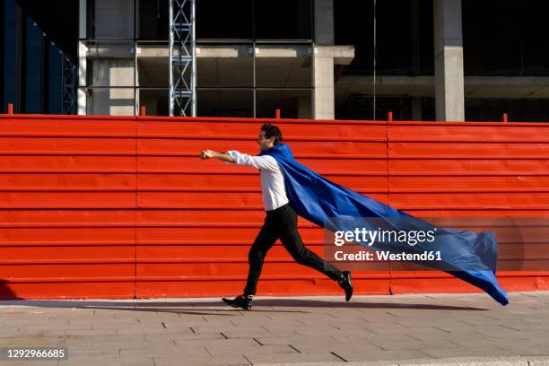 businessman wearing superhero cape running on pavement - mantel stockfoto's en -beelden