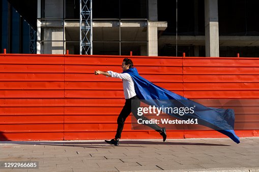 Businessman wearing superhero cape running on pavement Businessman wearing superhero cape running on pavement