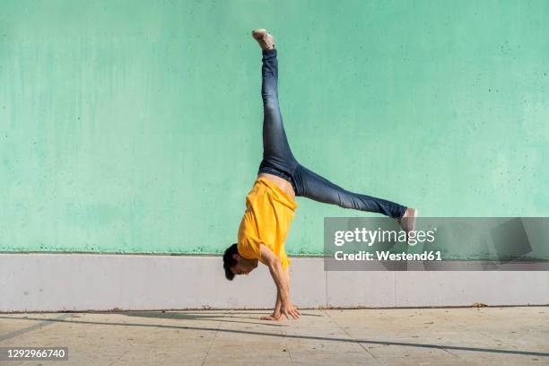 casual man doing handspring in front of green wall - handstand fotografías e imágenes de stock