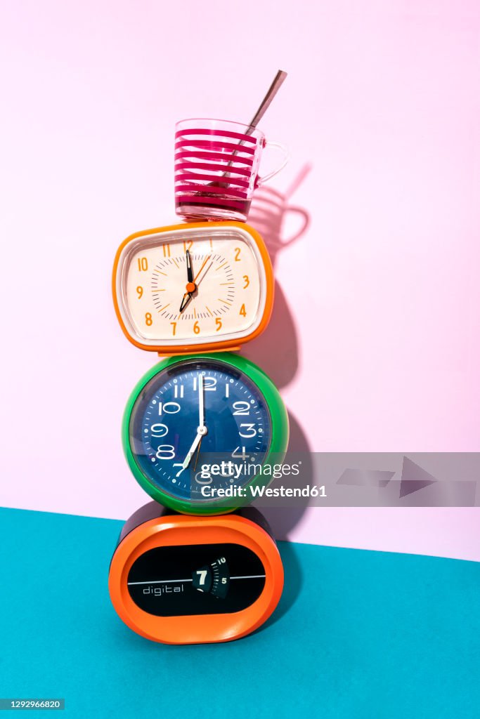 Coffee cup kept over clock stack against blue and pink background