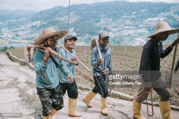 group of asian male farmers carrying their work tools walking back after work - ground staff imagens e fotografias de stock
