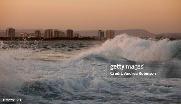 waves breaking in the golden late afternoon light which is reflected off the white foam at sunset with mooloolaba visible in the background, mooloolaba, sunshine coast, qld, australia. - mooloolaba stock-fotos und bilder