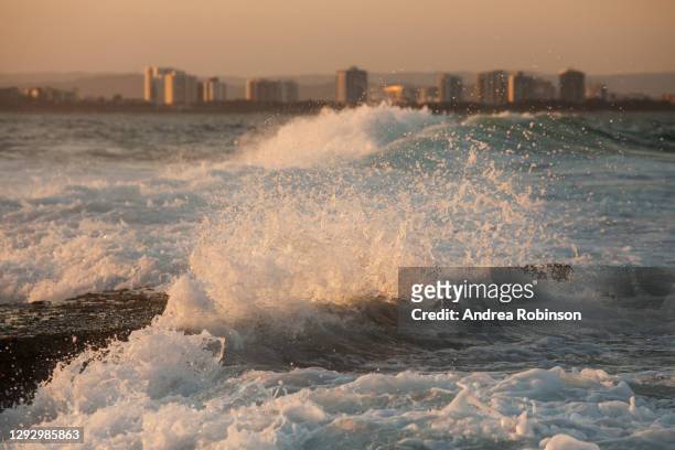 waves breaking in the golden late afternoon light which is reflected off the white foam at sunset with mooloolaba visible in the background, mooloolaba, sunshine coast, qld, australia. - mooloolaba stock-fotos und bilder