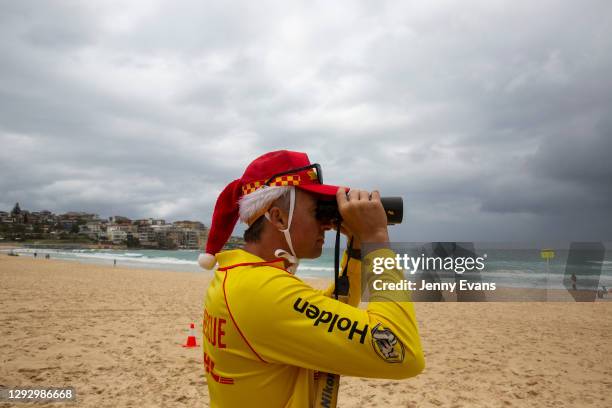 Surf rescue worker wearing a Santa hat looks through binoculars at Bondi Beach on December 25, 2020 in Sydney, Australia. December is one of the...