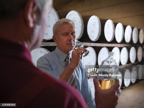 worker with whisky sample next to ageing whisky barrels in distillery - team spirit stock-fotos und bilder