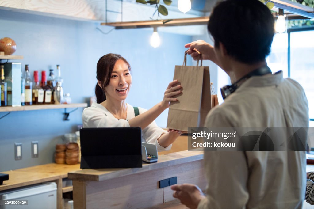 Female cafe staff giving a paper bag of take-out food to a male customer