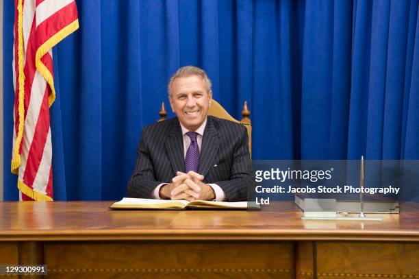 hispanic politician sitting at desk with american flag - mayor stockfoto's en -beelden