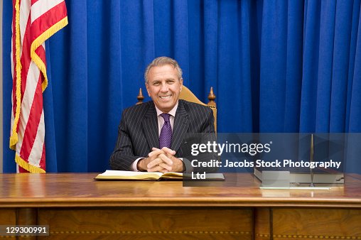 Hispanic politician sitting at desk with American flag