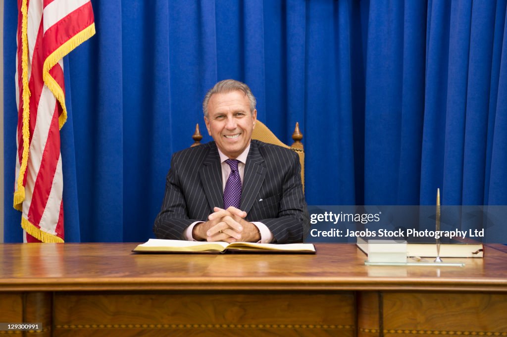 Hispanic politician sitting at desk with American flag