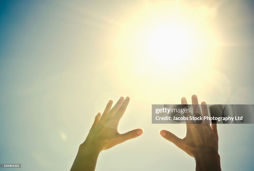 Mixed race woman's hands reaching toward sun