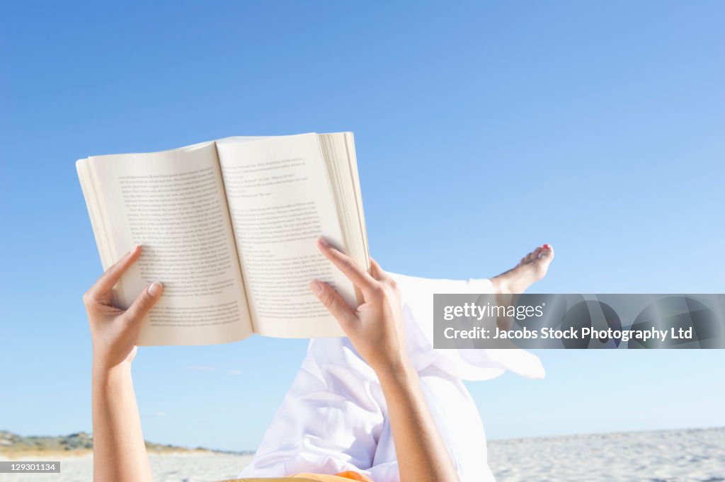 Mixed race woman reading book on beach