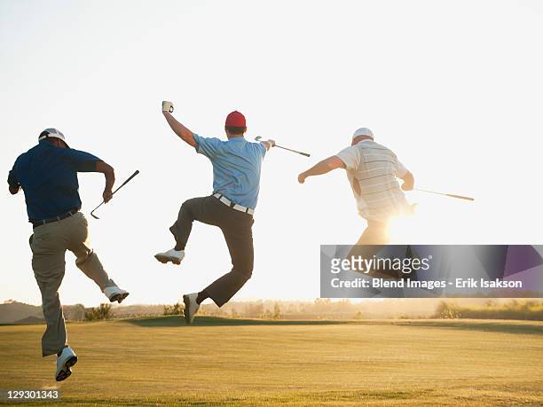 excited golfers jumping in mid-air on golf course - golf stock-fotos und bilder