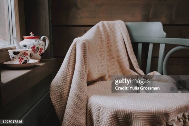 a gray chair with a beige blanket by the window. there is a teapot and a cup of tea on the window. - wool blanket stock pictures, royalty-free photos & images