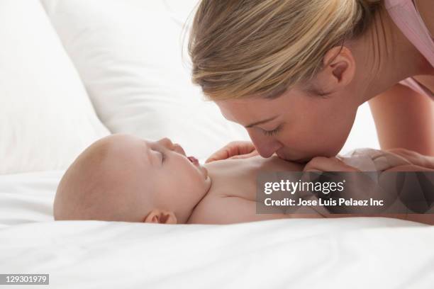 caucasian mother kissing baby girl - belly kissing stockfoto's en -beelden