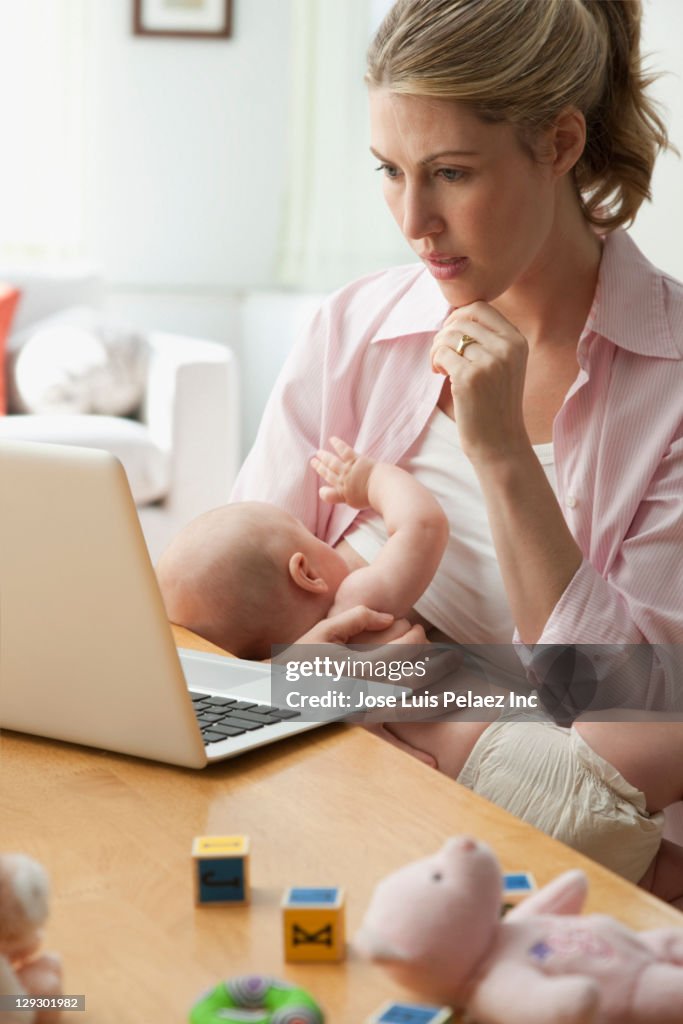 Caucasian mother breast feeding baby and working on laptop