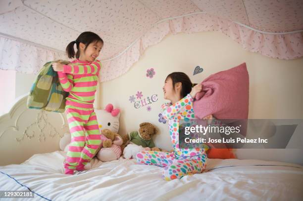 asian sisters having pillow fight in bed - pyjama stockfoto's en -beelden