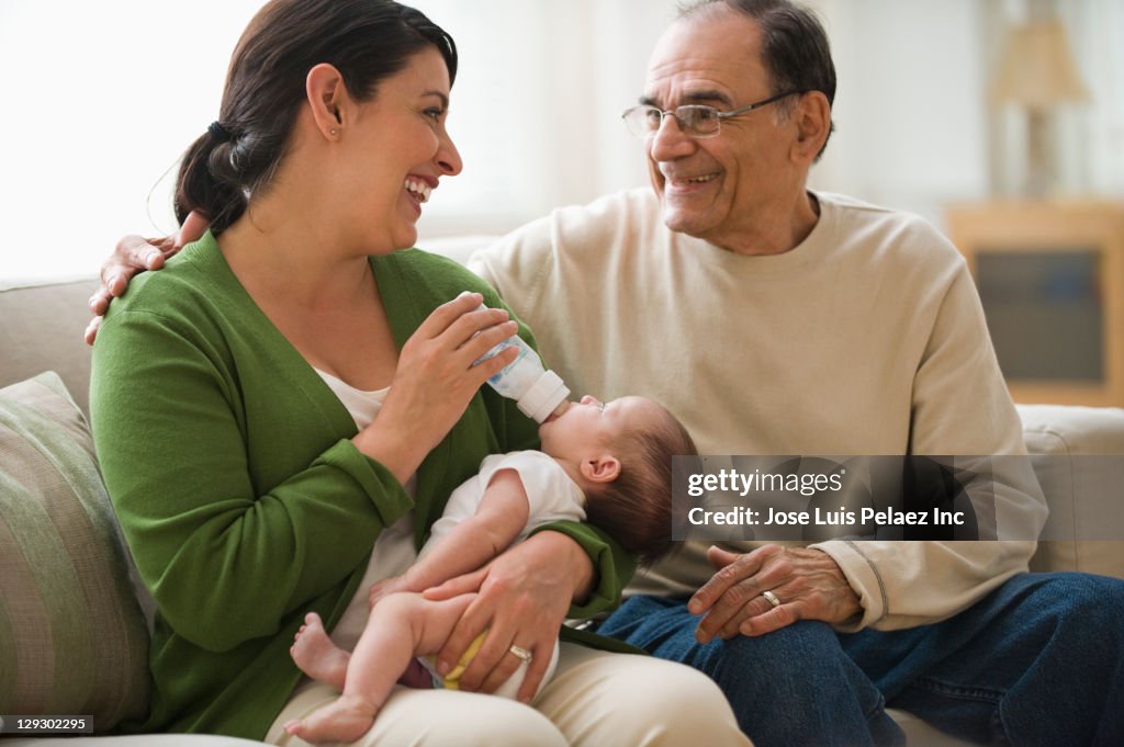 Grandfather watching Hispanic mother feeding newborn baby girl