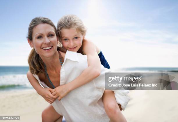 caucasian mother giving daughter piggy back ride on beach - west new york new jersey stock-fotos und bilder