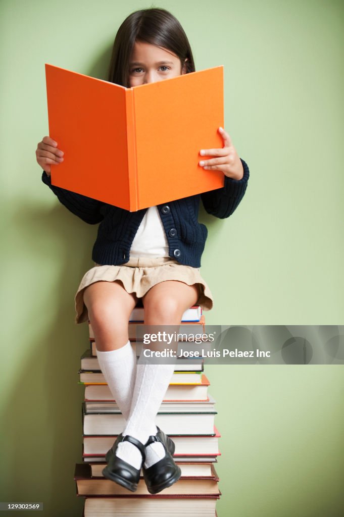 Mixed race girl sitting on stack of books reading book