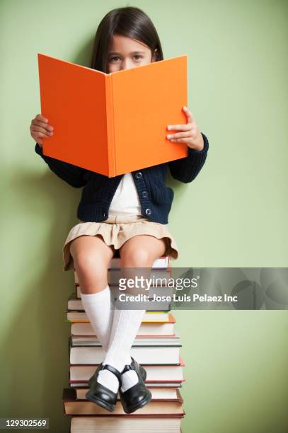 mixed race girl sitting on stack of books reading book - child reading a book stock pictures, royalty-free photos & images