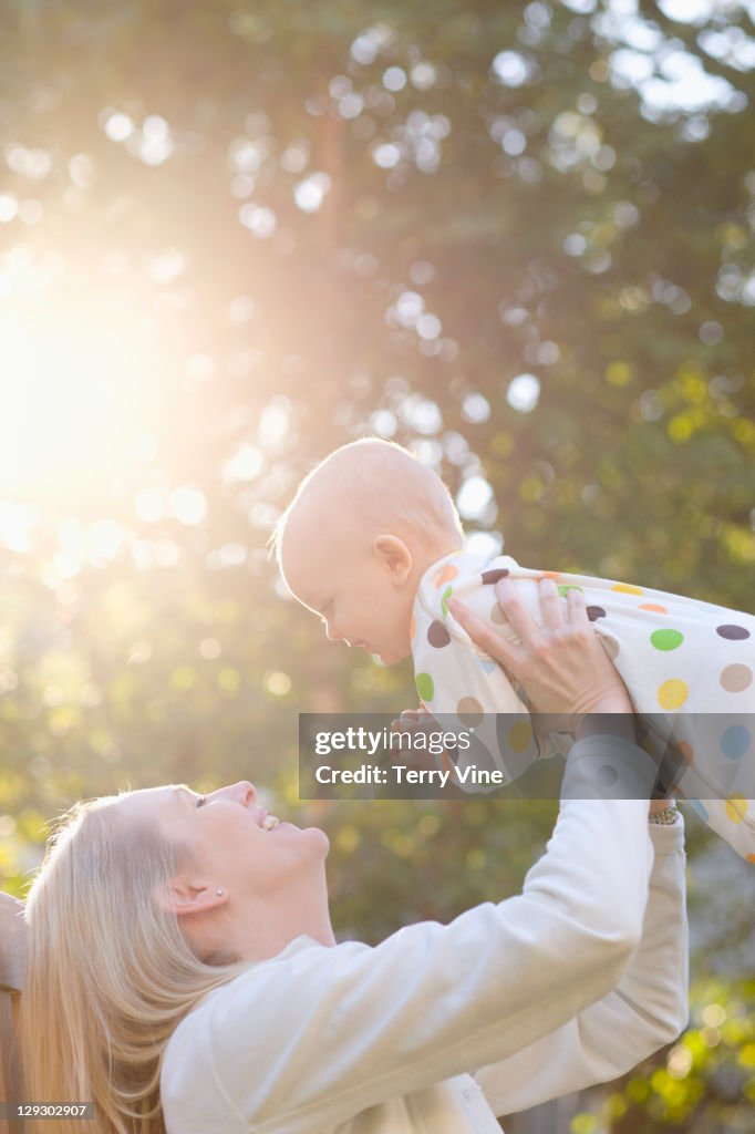 Caucasian mother lifting baby outdoors