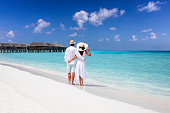 A hugging couple in white summer clothing stands on a tropical beach