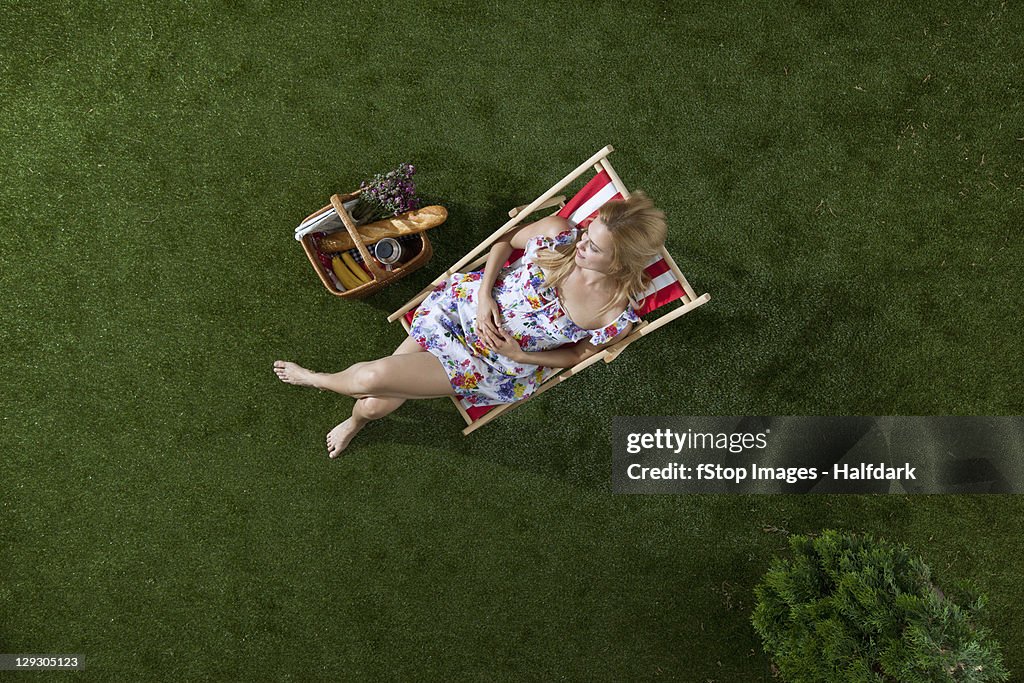 A woman sitting in the sun on a grass in a park with a picnic basket, overhead view