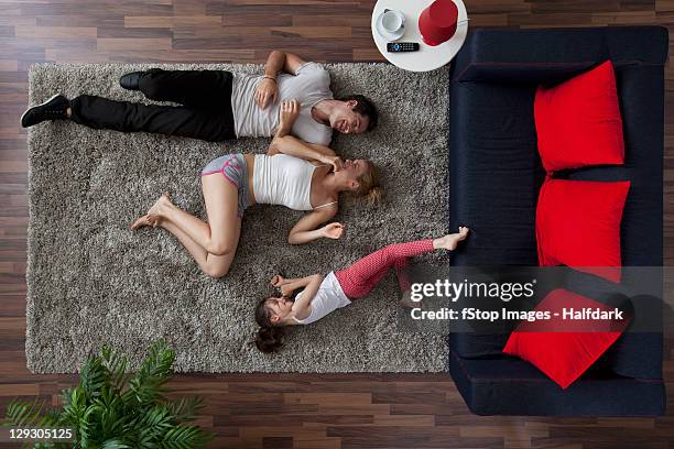a family of three happily lying on a living room rug, overhead view - lying on back girl on the sofa stock pictures, royalty-free photos & images