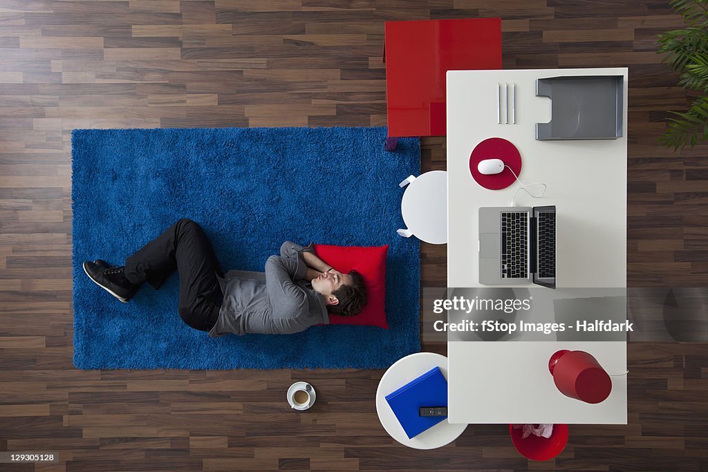 A businessman sleeping on a rug near his desk, overhead view