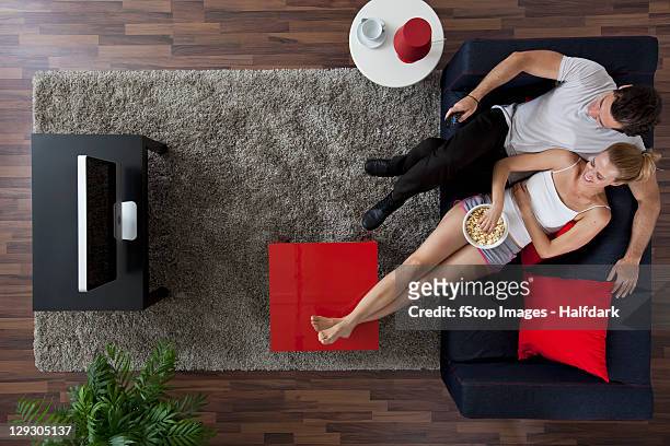 a cheerful couple watching tv and eating popcorn in their living room, overhead view - stop watch stock-fotos und bilder