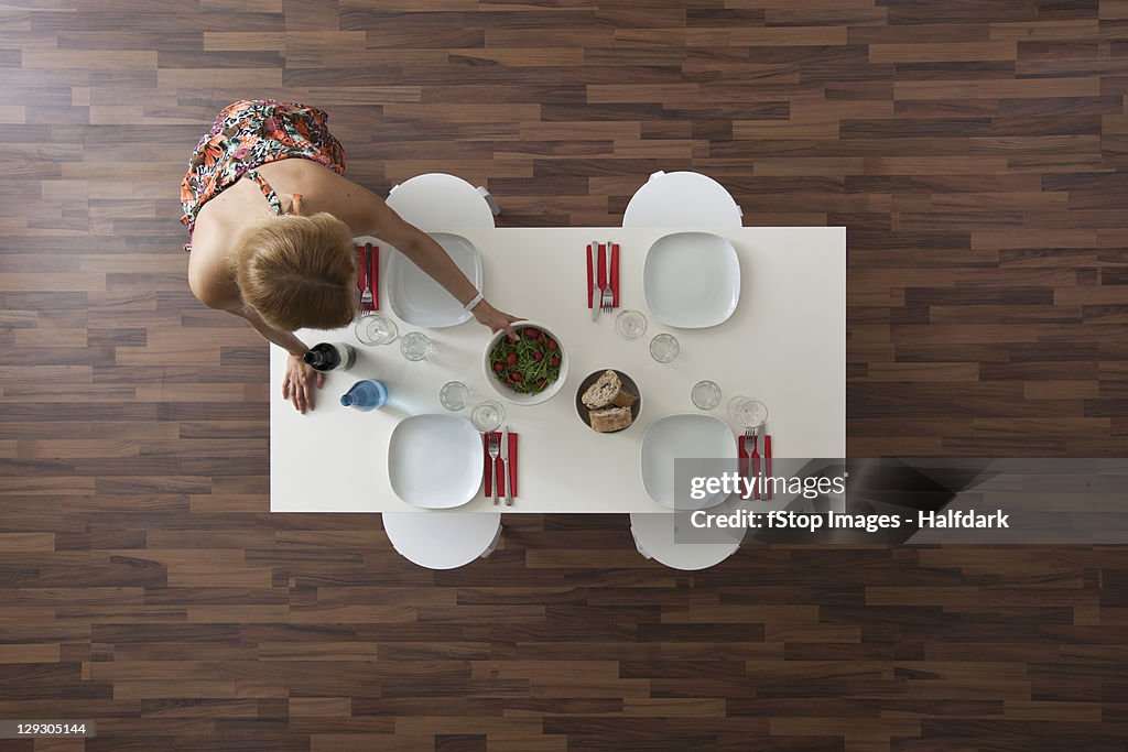 Woman setting dining room table for dinner party, overhead view