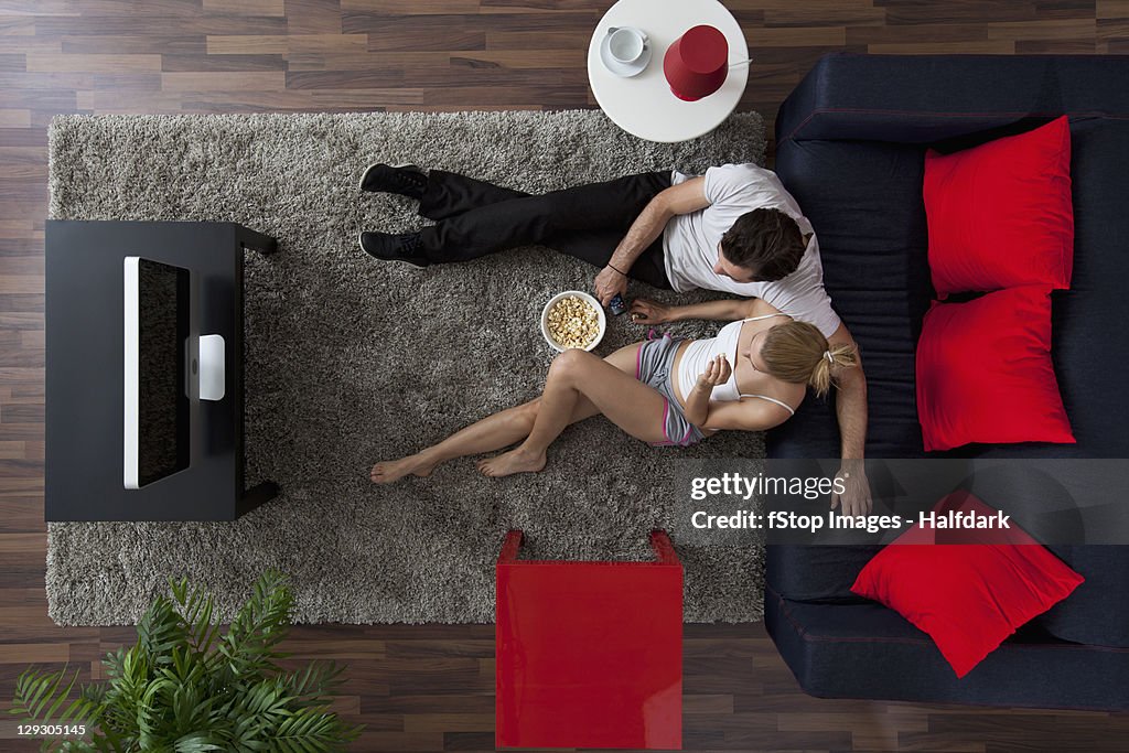 A couple eating popcorn and watching TV in their living room, overhead view