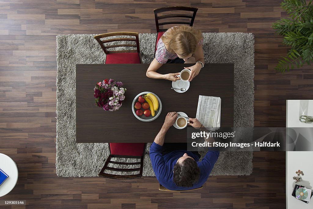 A couple having morning coffee together at a dining room table, overhead view