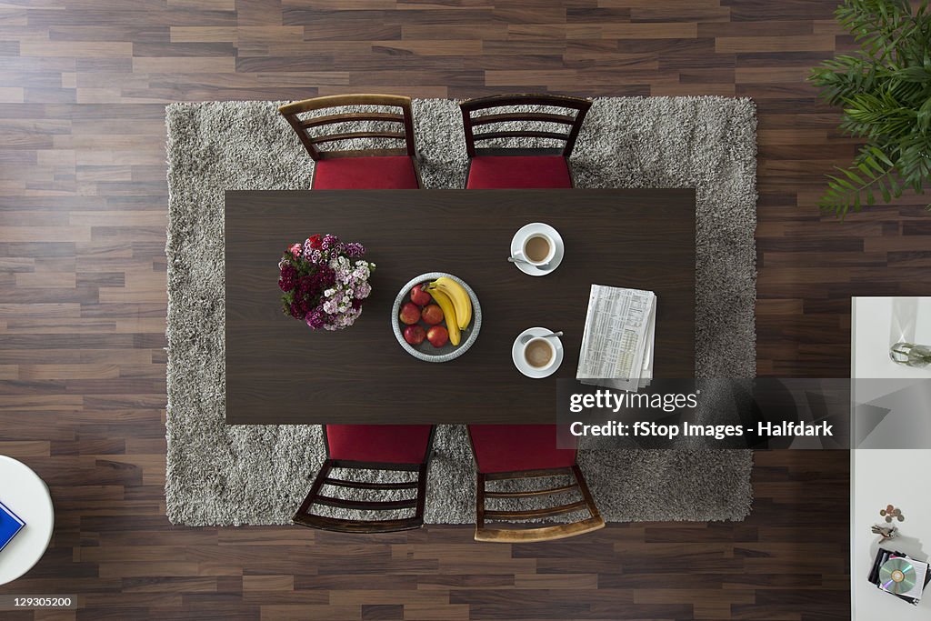 A dining table with coffee cups and newspaper, overhead view