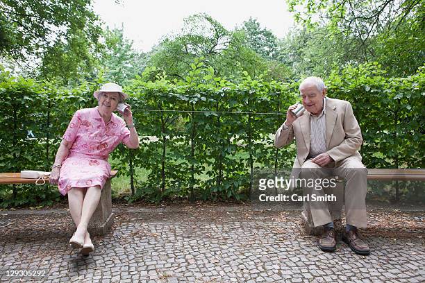 senior man and woman speak to each other on tin can phones in park - listening tin can stock pictures, royalty-free photos & images