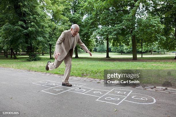 senior man playing hopscotch in the park - senior adult stock-fotos und bilder