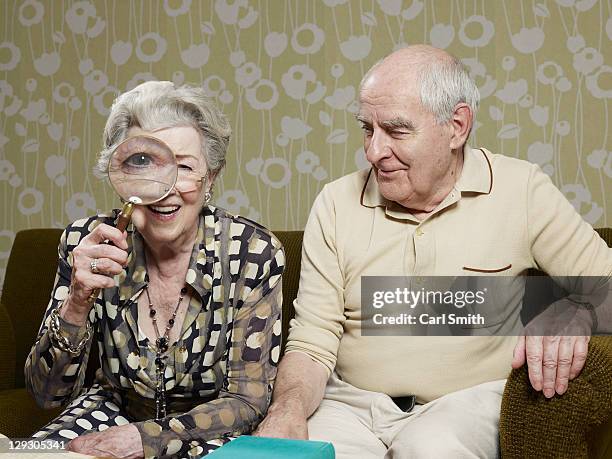 senior man amused as senior woman magnifies appearance of her eye with magnifying glass - vergrößerung stock-fotos und bilder