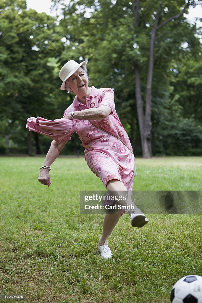 Senior woman kicks football n the park