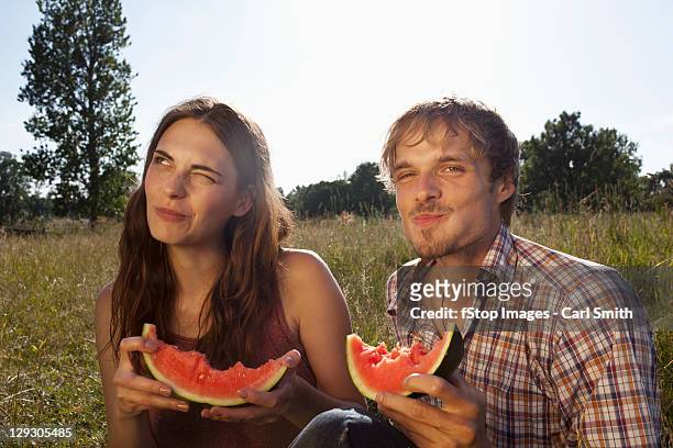 couple sitting eating melon in field - mâchonné photos et images de collection
